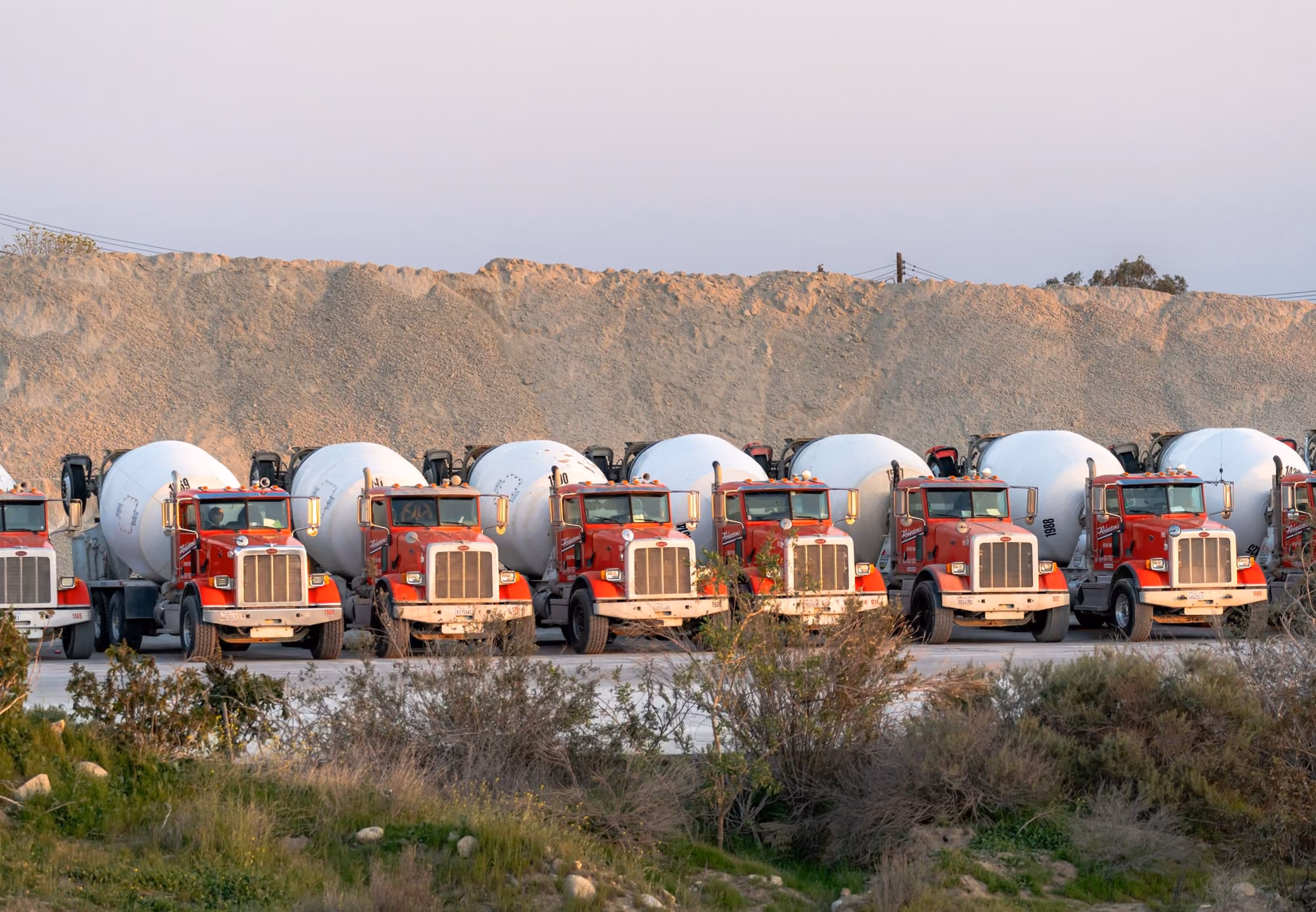 Camions toupies alignés sur leur parc, au pied d'un talus de sable